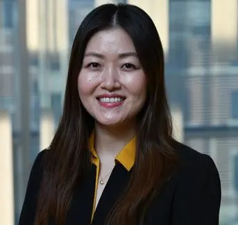 An asian woman with long dark hair wearing a dark jacket with a mango colored collar.