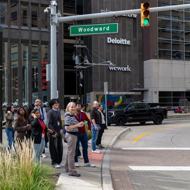 A group of people surrounded by buildings crossing Woodward Ave. in downtown Detroit.